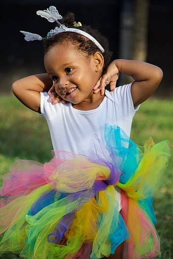 Charming young girl in a vibrant tutu smiling in a sunny outdoor setting. HD phone wallpaper