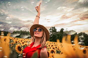 Cheerful woman enjoying a sunny day in a vibrant sunflower field while bubbles float around. HD wallpaper