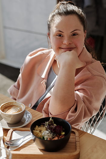 Smiling young woman with down syndrome enjoying breakfast and coffee at a café. HD phone wallpaper