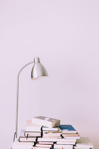 A stylish desk scene with a modern lamp illuminating a stack of books, embodying contemporary design. HD phone wallpaper