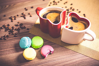 Heart-shaped coffee cups and colorful macarons on a wooden table for a romantic setting. HD wallpaper