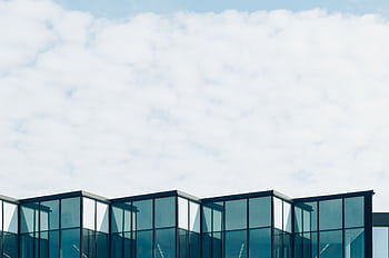 Low angle view of a modern glass building with a cloudy sky background, showcasing contemporary architecture. HD wallpaper