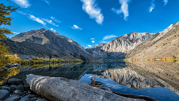 beautiful mirrored mountain lake, mirror, logs, sky, mountains, rocks, lake HD wallpaper