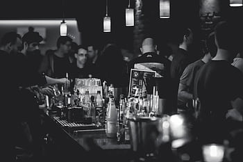 Black and white capturing the lively atmosphere in a bar with people socializing and a busy bartender serving drinks. HD wallpaper