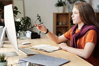 Teen girl in home office studying online using a computer and writing in a notebook. HD wallpaper