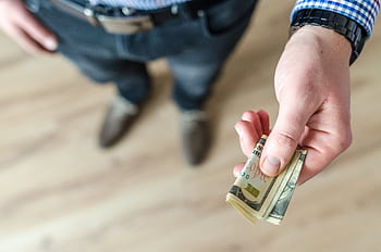 A close-up of a man's hand holding rolled US dollar bills, offering cash. HD wallpaper
