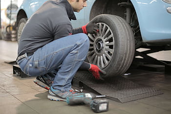 Mechanic changing a car tire indoors, using tools for vehicle maintenance. HD wallpaper