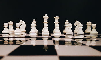 White chess pieces strategically placed on a board reflecting against a black background. HD wallpaper