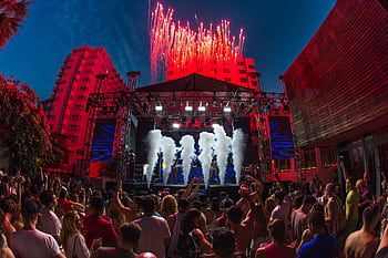 Lively outdoor music festival featuring a vibrant crowd, stage lights, and stunning fireworks display. HD wallpaper