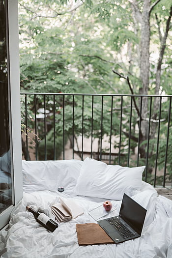 Relaxing on a cozy balcony with a laptop and wine bottle, surrounded by lush greenery. HD phone wallpaper