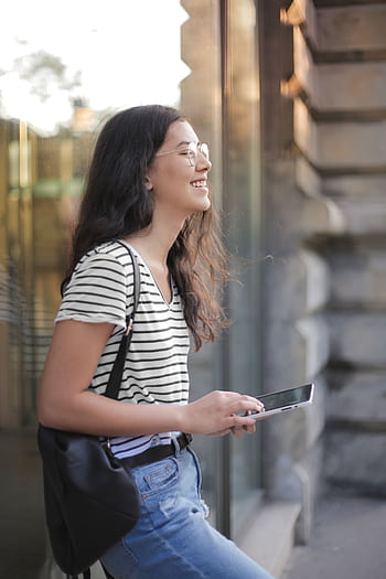 Cheerful woman in casual outfit browsing outside with a smile. HD phone wallpaper
