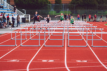 Women athletes compete in a hurdles race at a Victoria track event on a sunny day. HD wallpaper