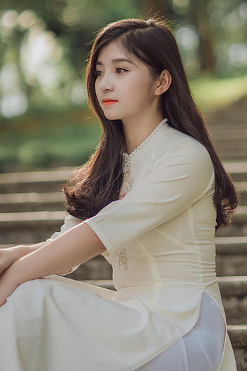 Asian woman in a white dress sitting on steps outdoors, showcasing elegance and beauty. HD phone wallpaper