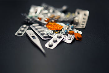 Close-up of various pills and a digital thermometer against a dark background. HD wallpaper