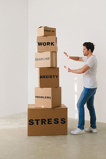A man in casual attire balances boxes labeled with stress-related words indoors. HD phone wallpaper