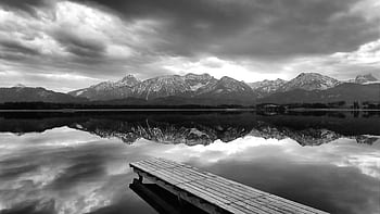 Monochrome landscape of mountains reflecting on a serene lake with a wooden pier. HD wallpaper
