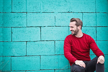 A cheerful man in a red sweater sits against a turquoise wall, enjoying a moment of happiness and laughter. HD wallpaper