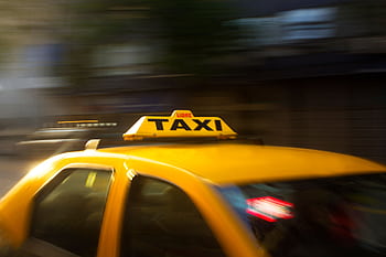 A vibrant yellow taxi with motion blur speeding through a nighttime city street. HD wallpaper