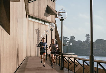 Two people jogging by the Sydney Opera House on a sunny day, capturing a healthy lifestyle. HD wallpaper