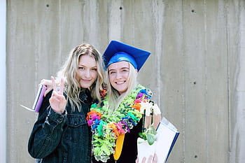 Two young women celebrating graduation outdoors with joy and vibrant colors. HD wallpaper