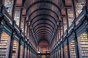 Explore the majestic architecture of an ancient library with classic wooden arches and towering book-filled shelves. HD wallpaper