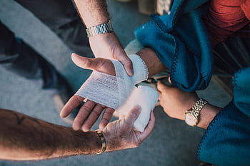 Close-up of two people bandaging an injured hand outdoors, focusing on first aid care. HD wallpaper