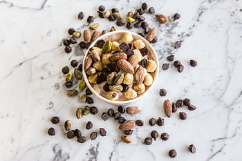 A bowl of mixed nuts and chocolate chips on a marble surface, perfect for healthy snacking. HD wallpaper