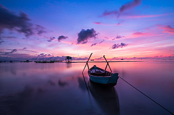 A tranquil tropical sunrise with a lone boat on calm waters. HD wallpaper