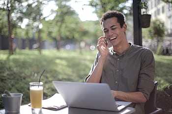 Smiling young man using a smart and laptop outdoors, enjoying casual work environment. HD wallpaper