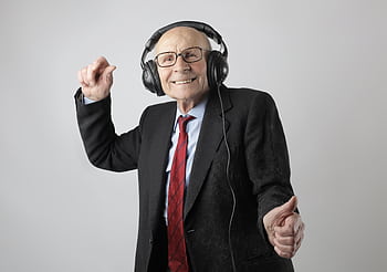 Happy senior man in formal attire delighting in music with heads on a white background. HD wallpaper