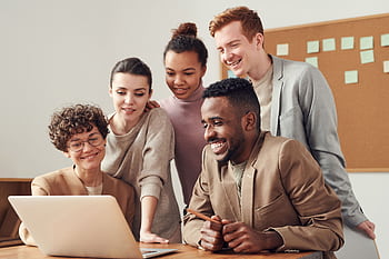 A group of diverse young professionals happily collaborating around a laptop indoors. HD wallpaper