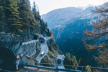 A breathtaking high angle view of a mountain road with a tunnel and a van driving through a pine tree forest. HD wallpaper