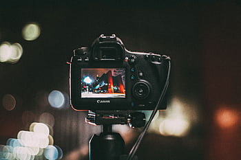 Close-up of a camera capturing a vibrant urban scene at night with a blurred bokeh background. HD wallpaper
