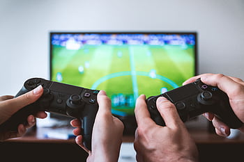 Close-up of hands holding gaming controllers in front of a TV. Engaged in a video gaming session. HD wallpaper
