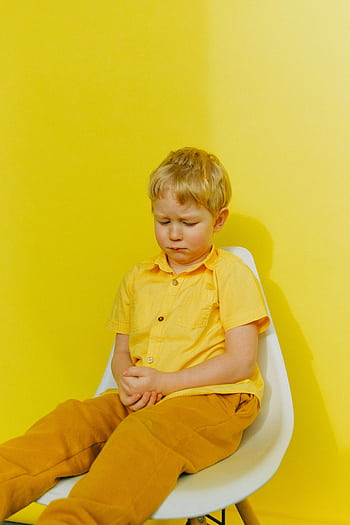 A young boy in yellow clothing displays sadness while sitting against a bright yellow background. HD phone wallpaper