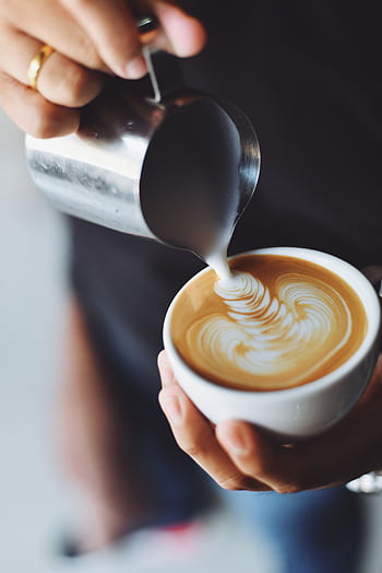 Close-up of hands pouring milk to create latte art in a coffee cup. HD phone wallpaper
