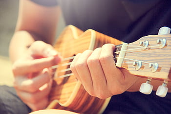 A person strums a wooden ukulele outdoors, enjoying leisure and music in the sun. HD wallpaper