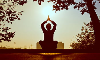 Silhouette of a person practicing yoga outdoors during sunrise, creating a calming atmosphere. HD wallpaper