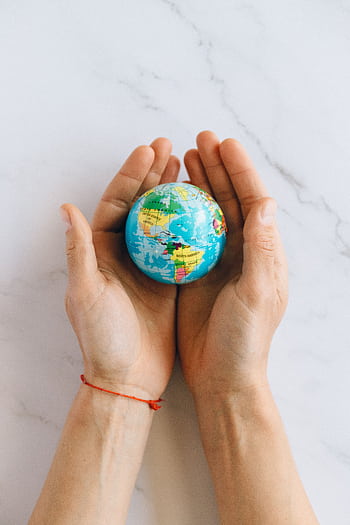 Close-up of hands gently holding a small globe representing global unity and care. HD phone wallpaper