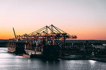 A serene view of cargo ships and cranes at a harbor during sunset, highlighting maritime industry. HD wallpaper