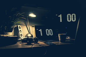 A dimly lit modern office desk with a laptop, heads, and speakers at 1:00 AM. HD wallpaper