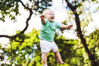 Happy baby wearing a green shirt being tossed in the air on a sunny day in the park. HD wallpaper