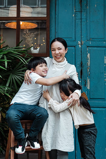 A joyful mother hugging her two children against a rustic blue door outdoors. HD phone wallpaper