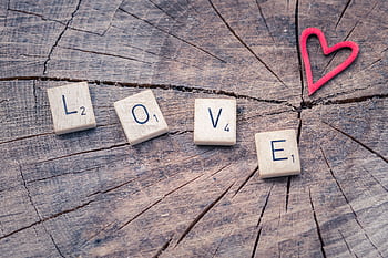 Scrabble tiles spelling 'LOVE' next to a heart shape on a wooden background. HD wallpaper