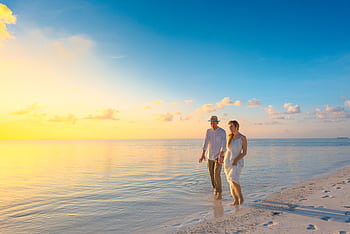 A couple enjoys a romantic walk on a sunny beach in the Maldives at sunrise. HD wallpaper