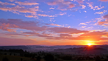 Stunning sunrise over rolling hills with colorful clouds and a vivid skyscape. HD wallpaper