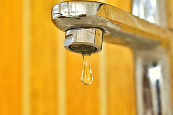 A close-up shot of a water droplet hanging from a stainless steel faucet, highlighting surface tension. HD wallpaper