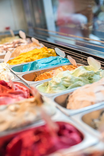 Colorful display of various gelato flavors in a modern ice cream parlor. HD phone wallpaper