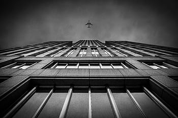 Dramatic perspective of a plane flying over a skyscraper in black and white. HD wallpaper