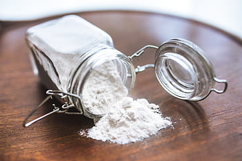 Glass jar tipped over with white flour spilling onto a wooden surface, ideal for baking themes. HD wallpaper